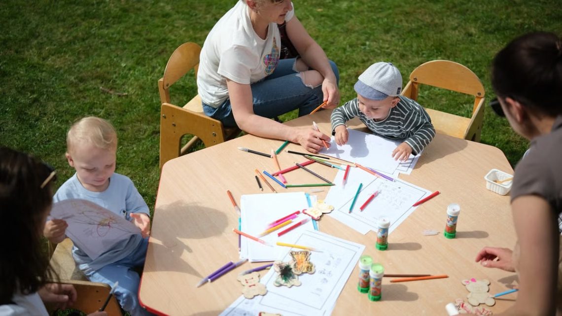 Children and parents engaging in outdoor art and craft activities with colored pencils.