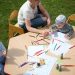 Children and parents engaging in outdoor art and craft activities with colored pencils.